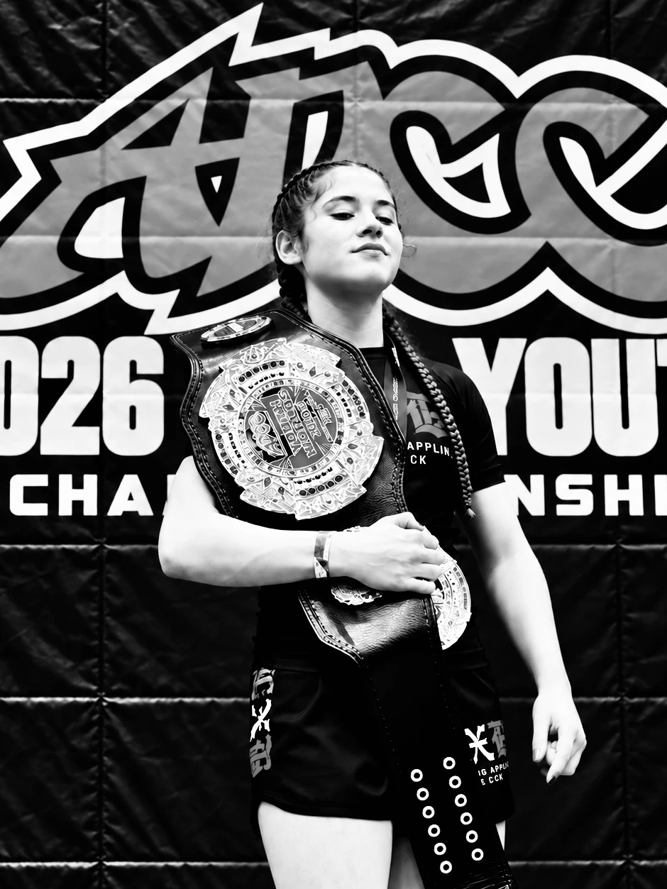 Young grappler holding an ADCC Youth World Championship belt in front of the event backdrop
