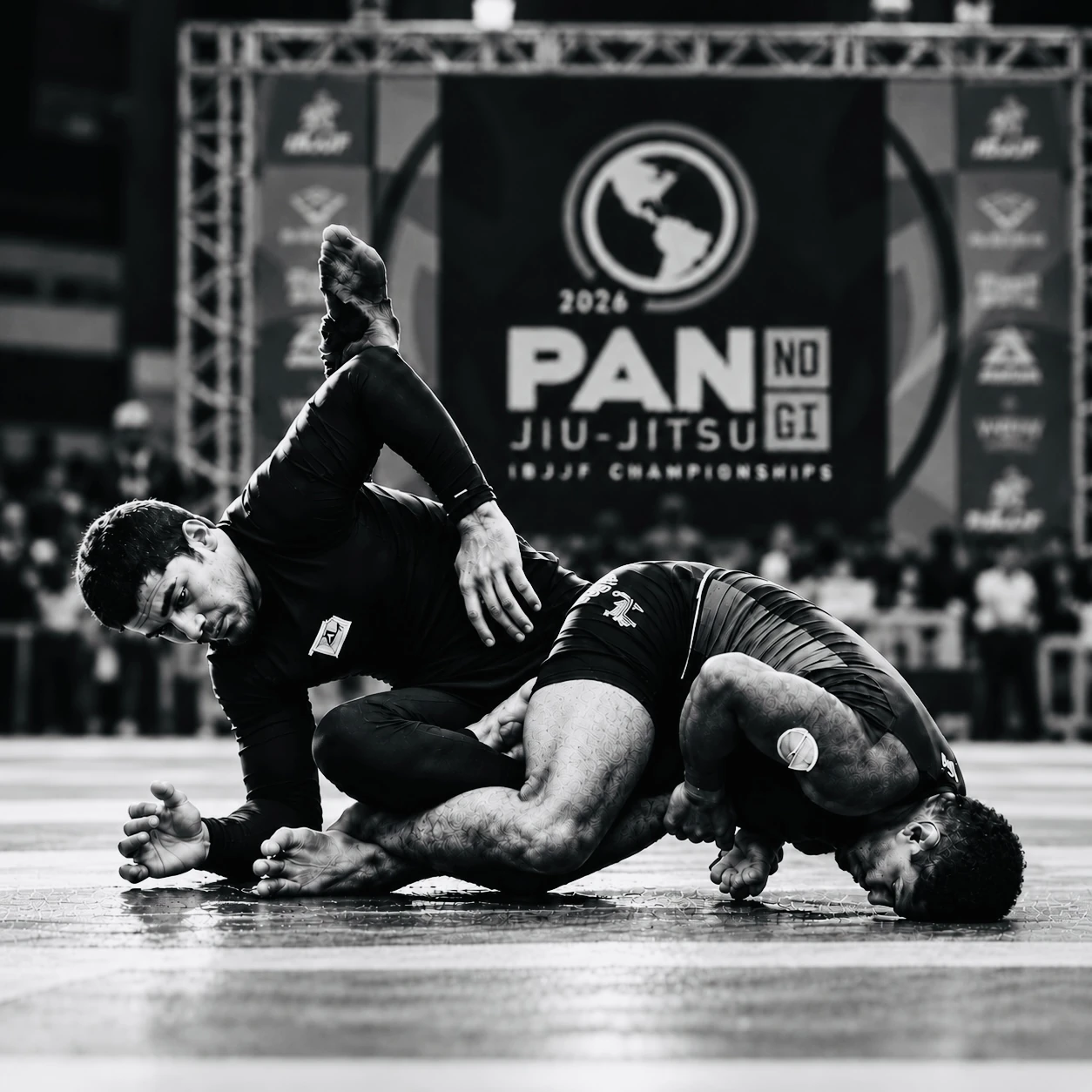 Two no-gi grapplers tangled on the mat in front of the 2026 Pan No-Gi Jiu-Jitsu banner